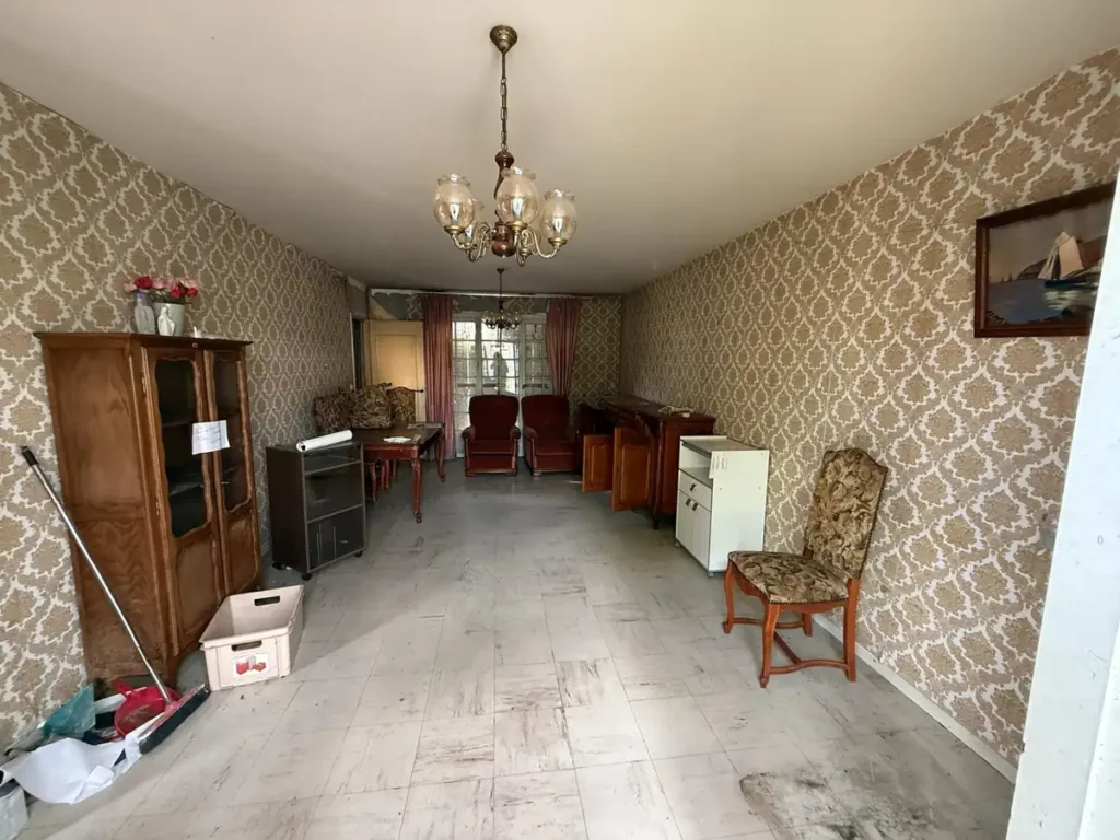 Séjour d’un pavillon avant rénovation : papier peint ancien, mobilier d’époque et sol usé