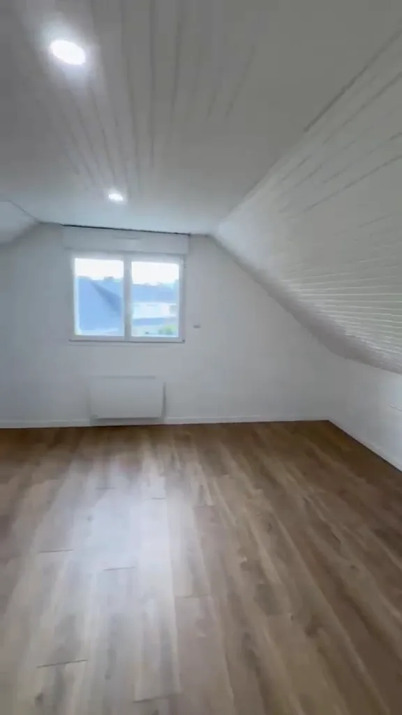 Chambre sous combles rénovée : lambris blanc, fenêtre neuve, radiateur et sol stratifié