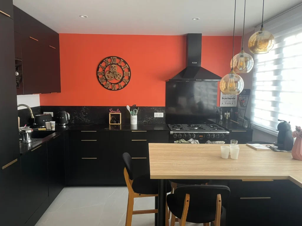 Cuisine ouverte noire mat avec bar en bois et suspensions dorées après rénovation accompagnée par Signature Travaux