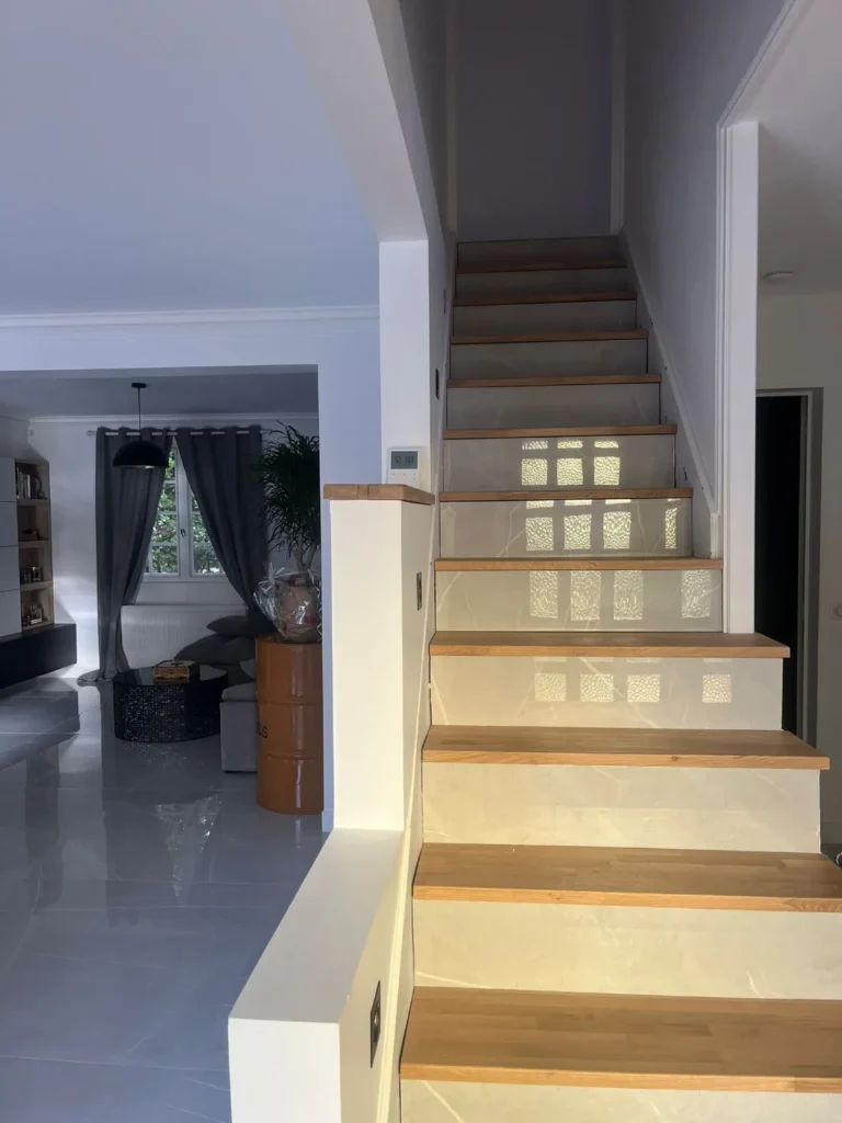 Escalier rénové avec marches en chêne massif et contremarches effet marbre ouvert sur la pièce de vie, rénovation accompagnée par Signature Travaux