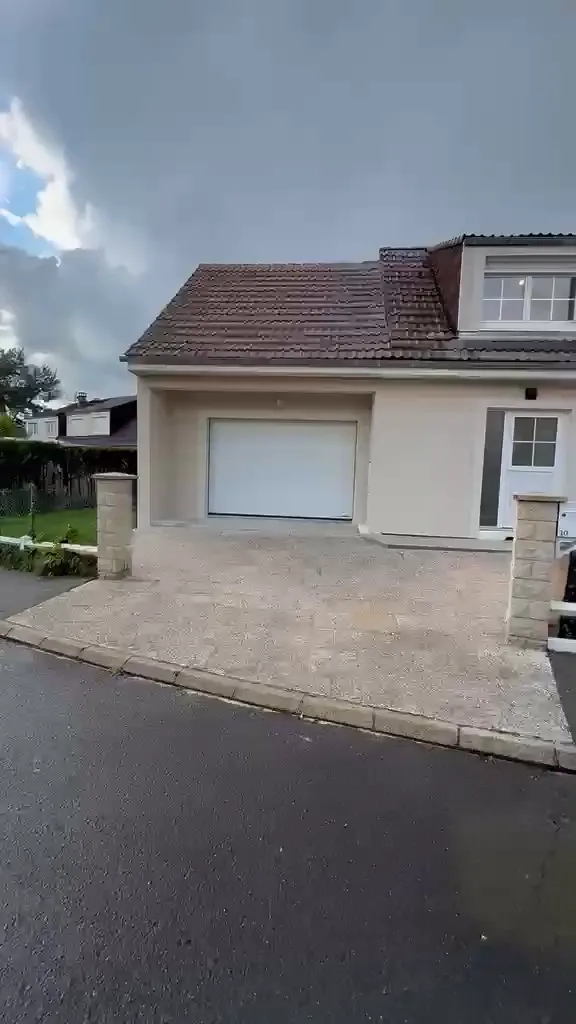 Façade d’un pavillon rénové : enduit clair, porte de garage blanche, toiture en tuiles et accès pavé