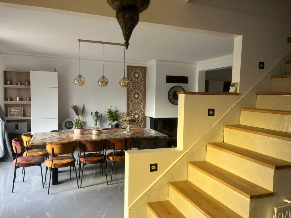 Pièce de vie décloisonnée avec cheminée, salle à manger et escalier rénové après travaux accompagnés par Signature Travaux