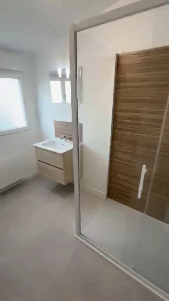 Salle d’eau rénovée dans un pavillon : douche vitrée, meuble vasque suspendu et sol gris
